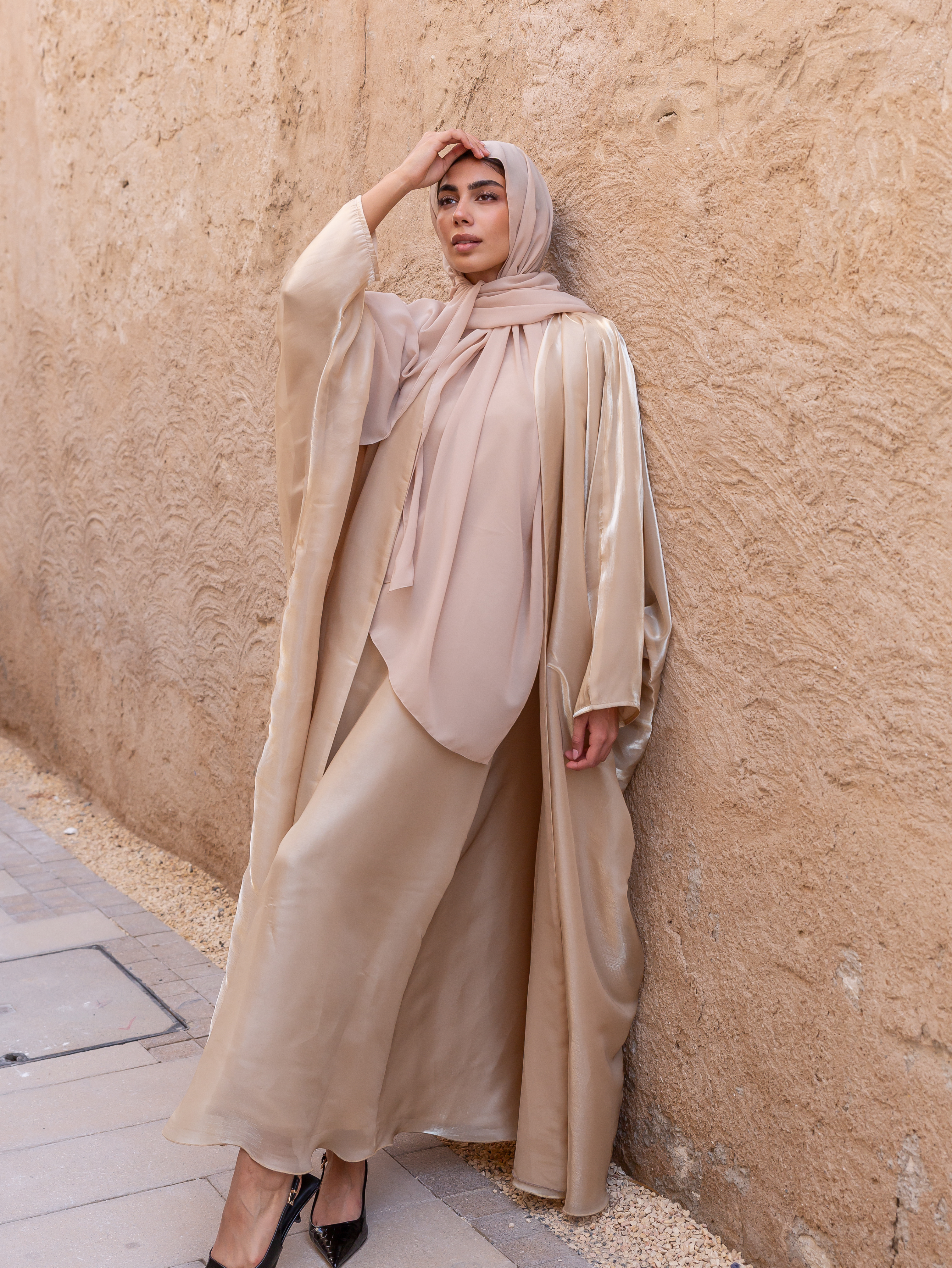 Woman in beige hijab and dress against a textured wall