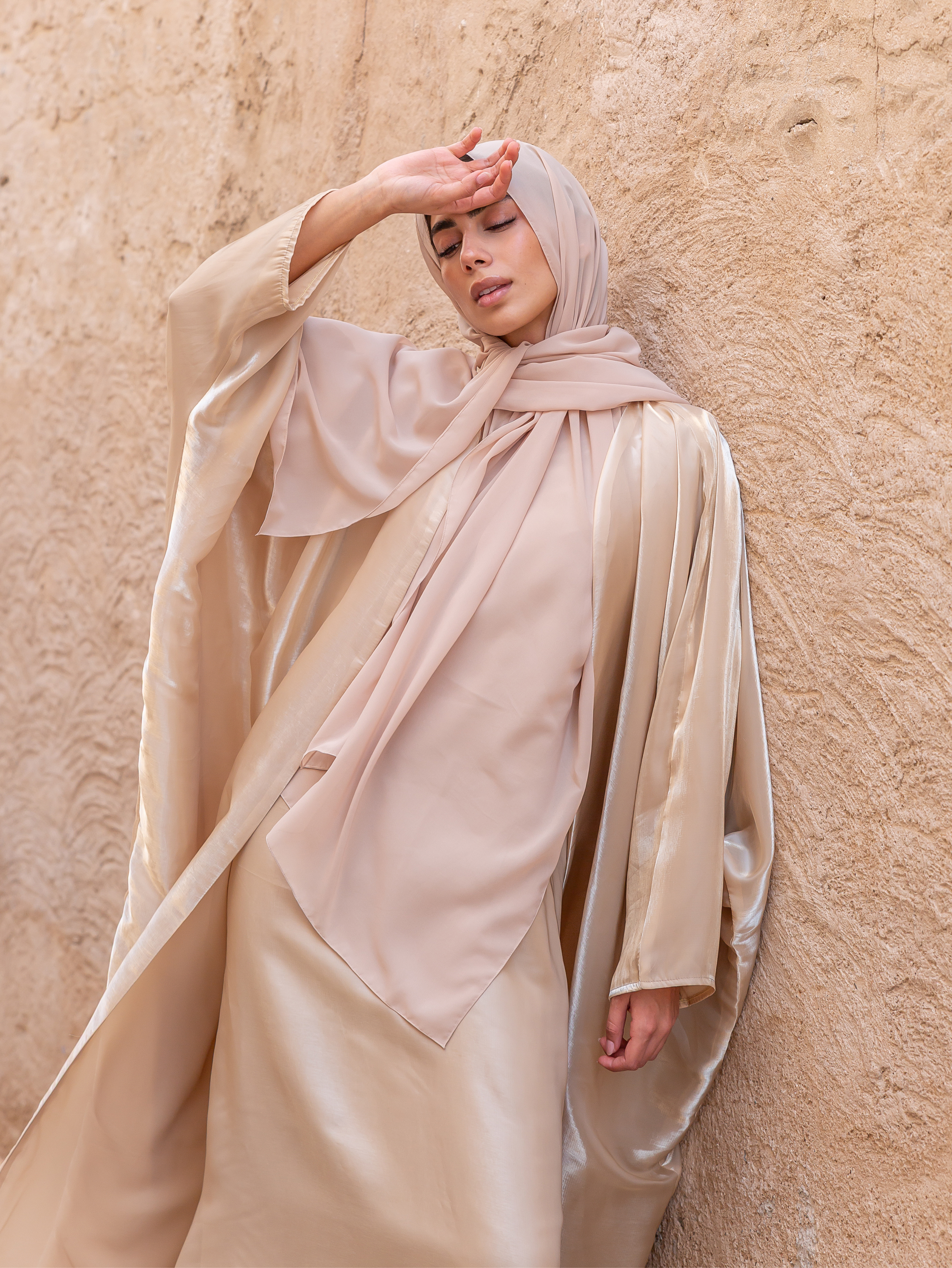 Woman wearing a beige hijab and dress against a beige wall